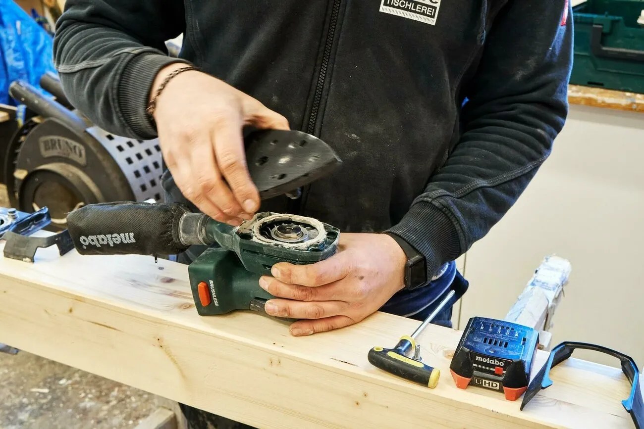 Handwerker hält den Akku-Multischleifer und setzt die Schleifplatte drauf.